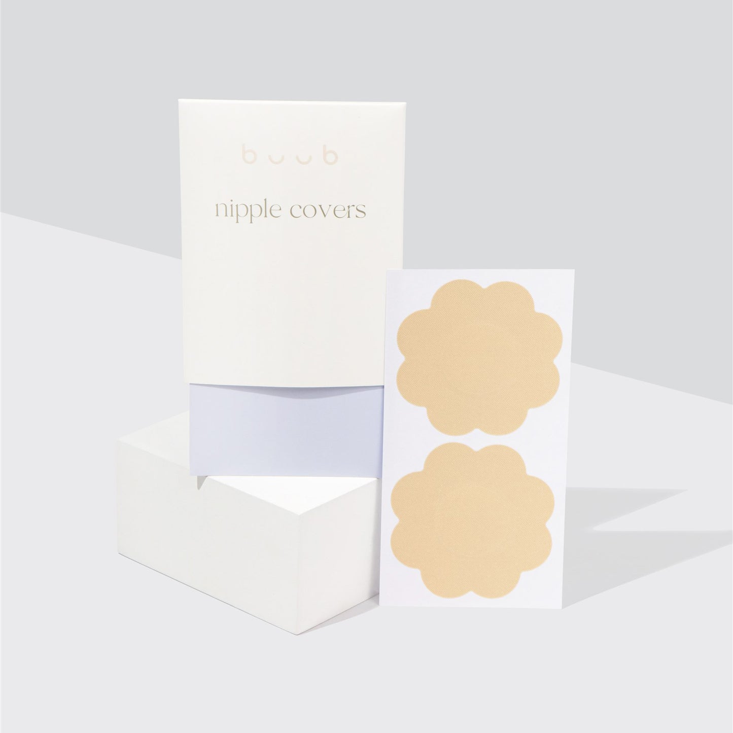Buub fabric nipple covers in a light nude shade for fair skin tones. A pair of the disposable, flower-shaped pasties is shown next to their elegant white and lilac envelope packaging.